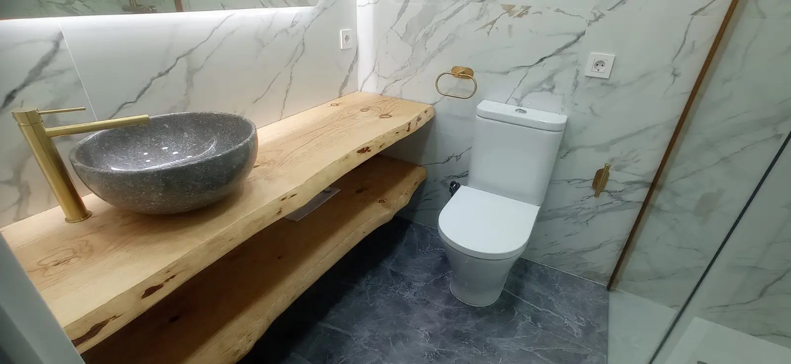 Reforma de baño con encimera de madera natural, lavabo de piedra y grifería dorada en Ripollet