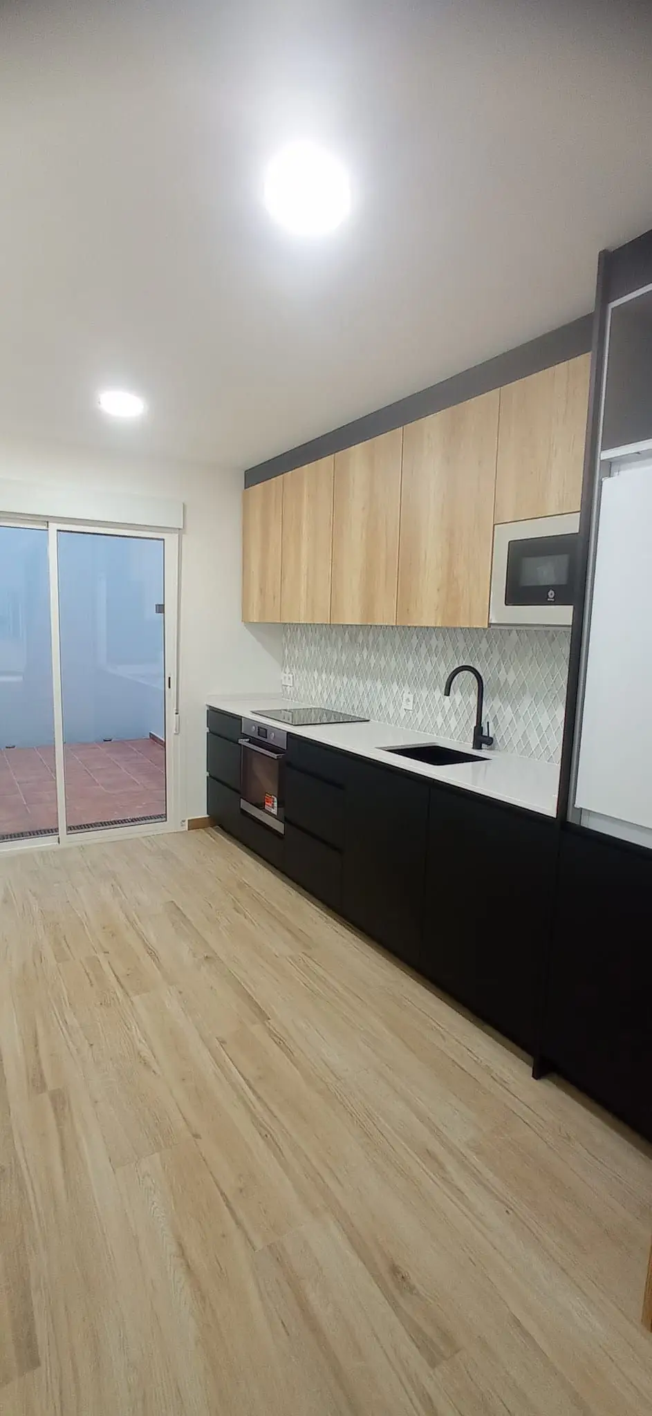 Reforma cocina con mobiliario negro mate, armarios superiores de madera y suelo laminado en Ripollet